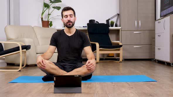 Man Meditating in Lotus Yoga Pose and Looking at a Digital PC