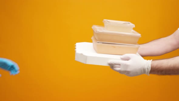 People's Hands Passing Each Other Packed Boxes with Food Delivery Against Yellow Studio Background