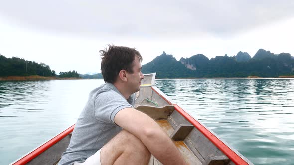 Happy Smiling Man Sitting on Wooden Boat and Sailing on Morning Blue Lake