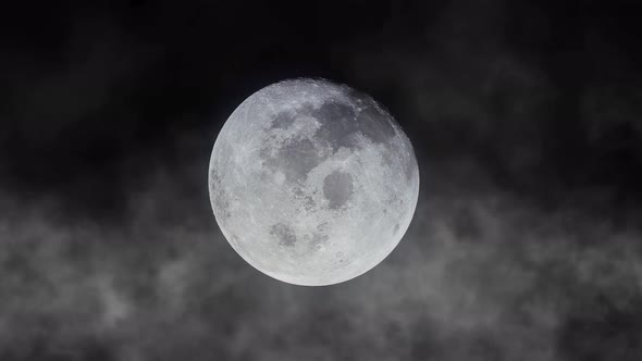 The bright full moon on the dark sky with clouds during a storm at night.