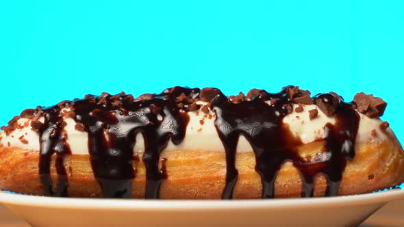 Sweet Eclair with Chocolate Sprinkles Rotating on a Wooden Table on a Blue Background