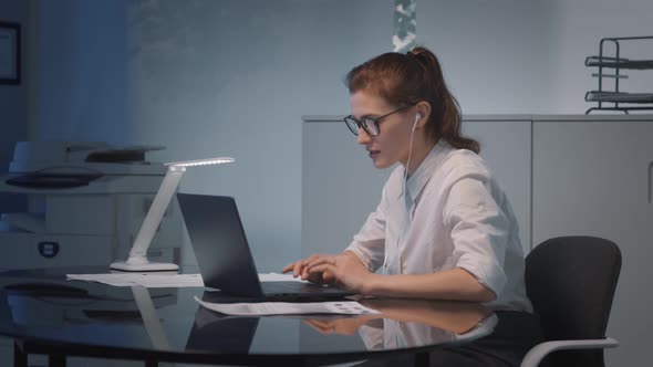 Attractive Caucasian Businesswoman in Earphones Talking During Video Call at Office Workstation