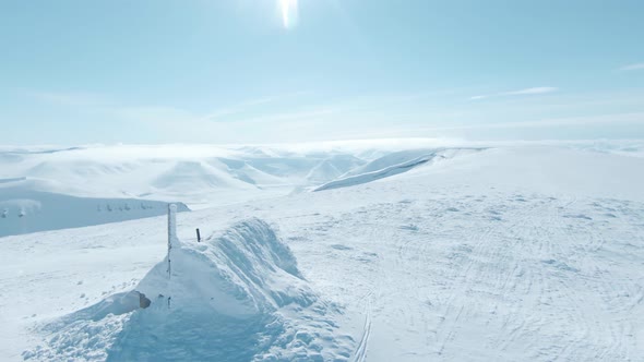 Old hut covered in thick layer of snow on Svalbard mountain top, aerial view