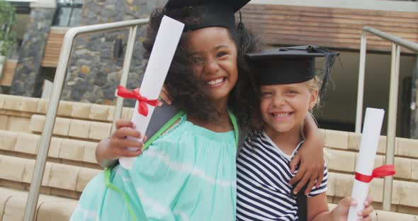 Video of happy diverse girls wearing graduation hats and holding diplomas