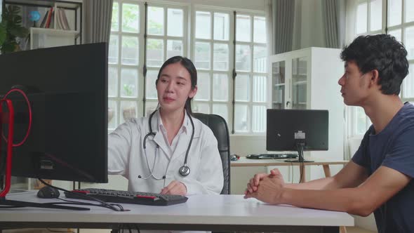 Asian Woman Doctor Is Talking With Young Male Patient During Consultation In A Health Clinic