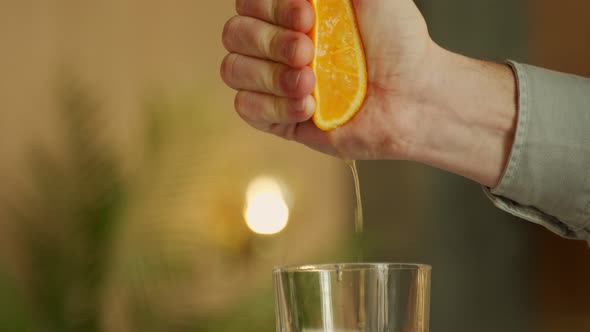 Hand of a Young Man Squeezes Juice From an Orange Into a Glass