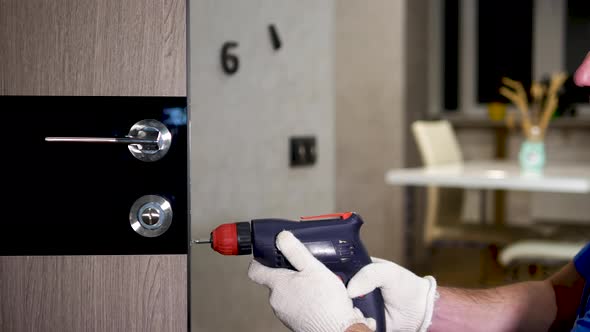 A Carpenter In A Special Uniform Repairs The Lock Of The Front Door. Remove The Screw From The Lock.