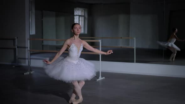 Wide Shot Slim Agile Ballerina in White Dress Tutu Performing Arabesque Movements in Dark Studio