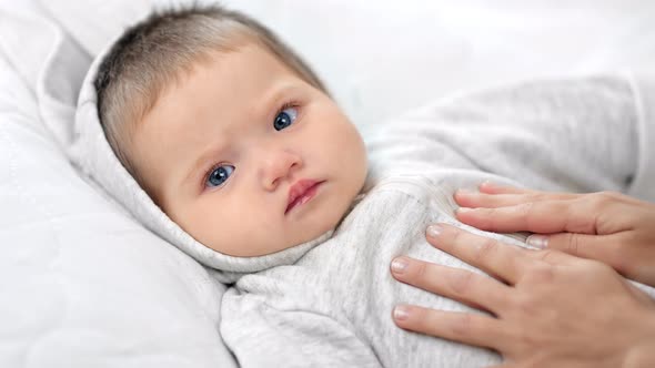 Focused Face of Beautiful Little Baby Lying on Bed During Caress By Female Hand Looking at Camera