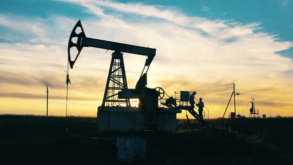 Oil Pumping Constructions and Two Technicians at Sunset