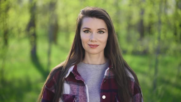 Portrait of a Young Brunette on a Background of Green Trees