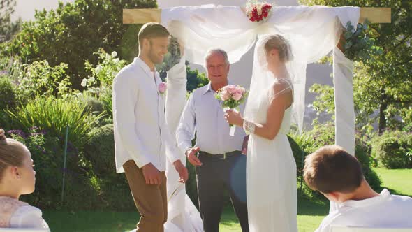 Caucasian bride and groom standing at outdoor altar with wedding officiant during ceremony