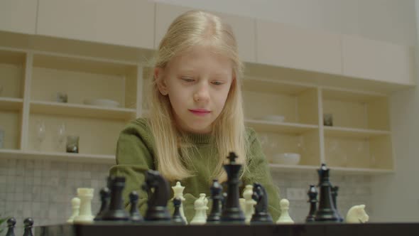 Thoughtful Cute School Age Girl with Hearing Loss Playing Chess Indoors