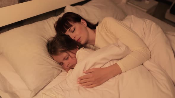 Young Mother and Little Daughter Sleeping in Bed Together