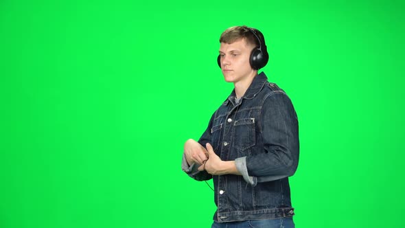 Man in Big Headphones Goes, Listening Music and Dancing with Smartphone on Green Screen at Studio