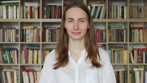 Portrait of Young Librarian Woman Smiling Looking at Camera in Library Bookshelf Background