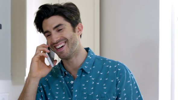 Smiling man talking on the mobile phone in kitchen