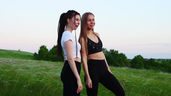 Two Young Women Standing in the High Grass and Watching the Sunset  Pointing at the Sky