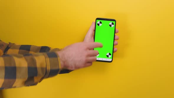 Male hand holding a cellphone with horizontal green chroma key screen.