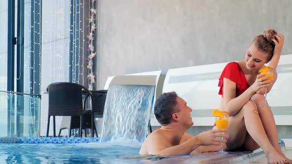 Joyful Couple Smiles Holding Cocktails in Hands at Pool