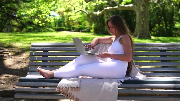 Well Looking Middle Aged Woman Typing on Laptop Keyboard Outdoors on Bench in the Park