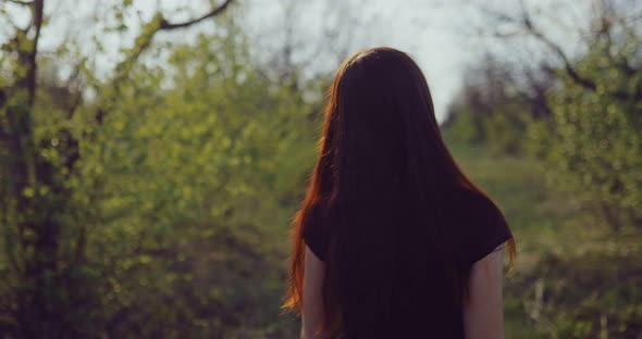 Brunette Woman with Long Hair is Walking in the Garden in Spring