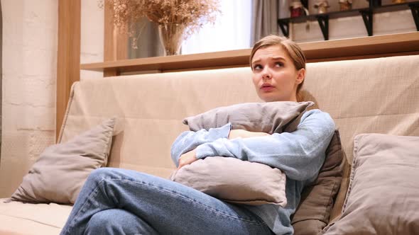 Sad Young Woman Feeling Scared and Confused Sitting on Sofa