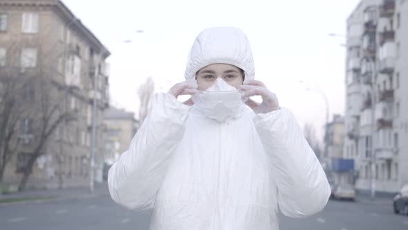 Middle Shot of Serious Caucasian Woman in Antiviral Suit and Face Mask Putting on Protective