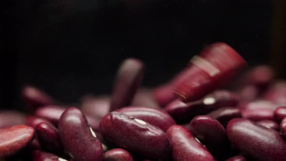 Closeup of Falling Down Red Beans Into Glass Jar on Black Background