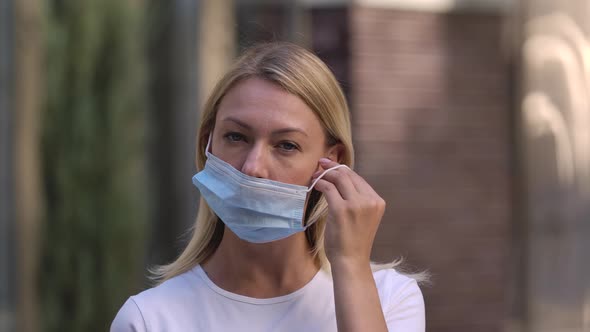 Portrait of Pretty Young Woman Looking Into the Camera and Putting on Medical Mask on Face for