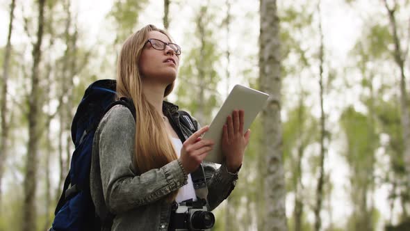 Young Caucasian Woman Backpacker Using Tablet for the Orientation in the Forest. Low Angle Shot