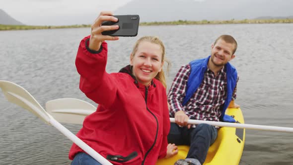 Caucasian couple having a good time on a trip to the mountains, kayaking together on a lake, taking