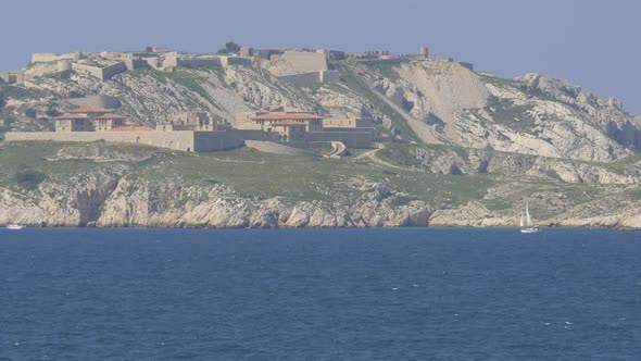 A boat sailing by an island with fortification walls