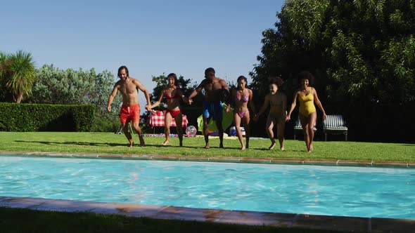 Diverse group of friends having fun jumping into a swimming pool