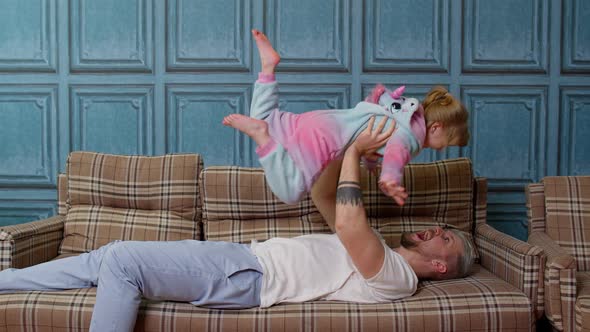 Child Girl Flying As Airplane Playing Game Laughing with Young Father Relaxing on Sofa at Home