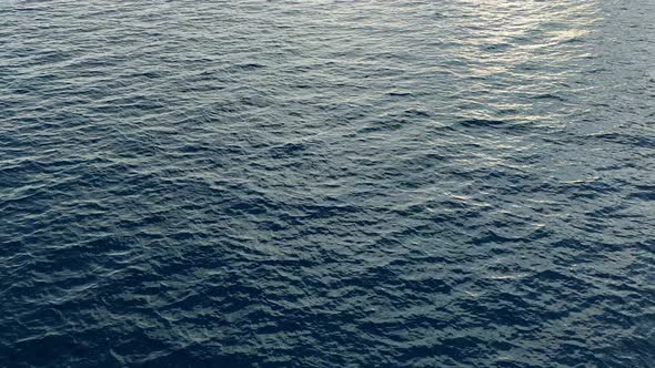 Camera hangs over the blue open calm sea water 