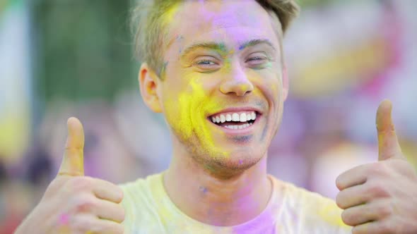 Handsome Man Showing Thumbs-Up, Happy Face Covered in Colored Powder, Closeup