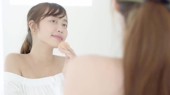 Beautiful young asian woman applying powder puff at cheek makeup of cosmetic looking mirror.