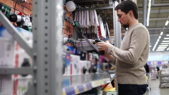 Young Man Choosing a Drill in the Hardware Store in Big Supermarket