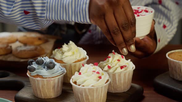 African American Chef Decorating Cupcakes with Berries and Confetti Closeup