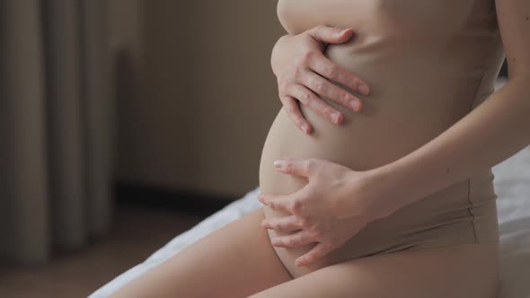 Close Up of Pregnant Woman in Beige Body Petting Her Belly in Bed