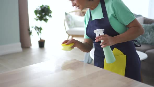 Mature Caucasian Woman Wipe Table Using Spray Bottle in Home Room