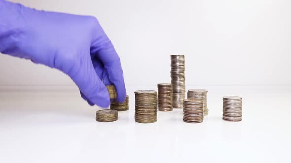 A hand in medical gloves puts coins into a column. Investment concept