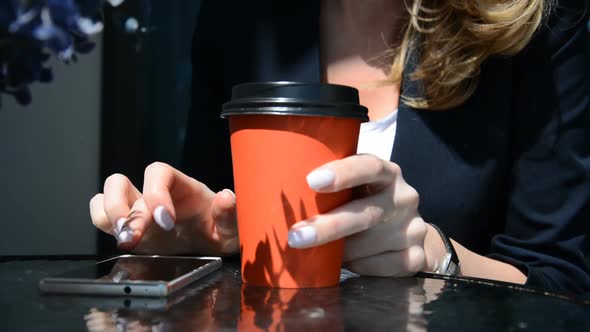 Closeup of Beautiful Young Female Hands Scrolling Smart Phone in Cafe with Cup of Hot Coffee at