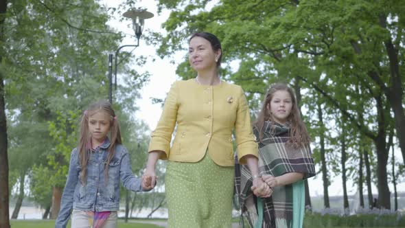 Portrait Mature Grandmother Walking in the Beautiful Green Park with Two Cute Granddaughters Holding