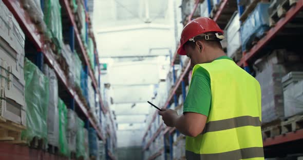 An Engineer Inspects a Cargo on Shelves in a Warehouse and Notes on a Tablet