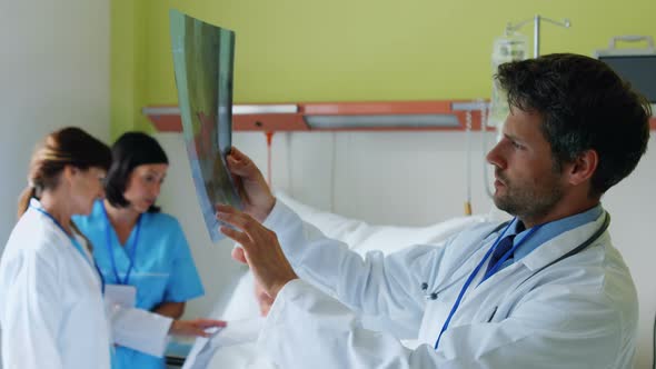 Doctor examining x-ray while nurse interacting with patient in background