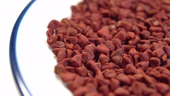 Achiote seeds. Annatto grains in white plate. Red natural culinary dye. Mexican seasoning