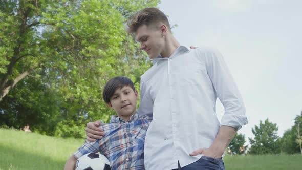 Adorable Child Holding Soccer Ball Hugging with the Dad Looking in Camera in the Park. Family