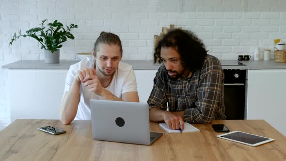 Two Young Freelance Guys Work Remotely At Home on an Online Project, Using a Laptop and a Tablet